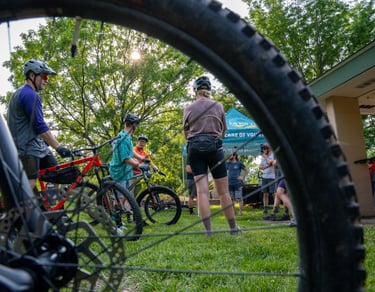 Photo of people standing with their bikes in the background of a close up shot of a bike tire