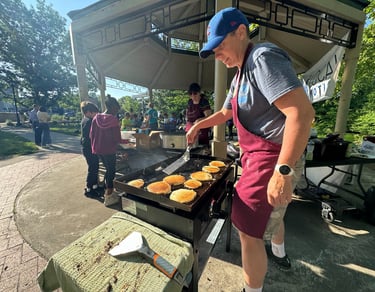 Kids in the background of a person flipping pancakes on a griddle in a park