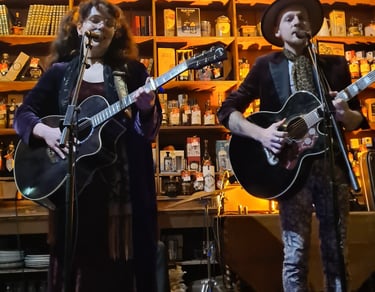 A folk music duo performing live with acoustic guitars in a rustic pub setting with warm lighting.