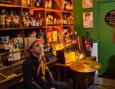 A musician plays a cajon drum during a live session in a cozy Irish pub with whiskey shelves.