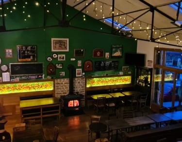 Cozy Irish pub interior with green walls, fairy lights, a wood-burning stove, and seating areas.