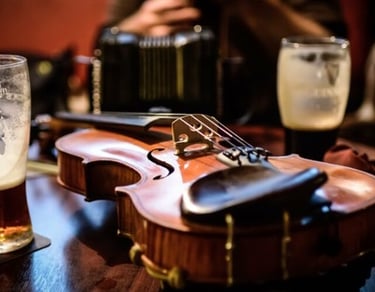 A wooden fiddle sits on a pub table alongside pints of beer and an accordion.