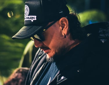 Un hombre con una gorra negra tipo trucker de Linkin Park y gafas de sol, mirando hacia abajo 