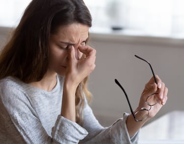Tired woman holding glasses and rubbing eyes to relieve digital eye strain and headache.