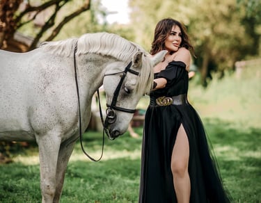 Model in black dress posing beside a white horse in nature, photographed by Fred Art Studio.