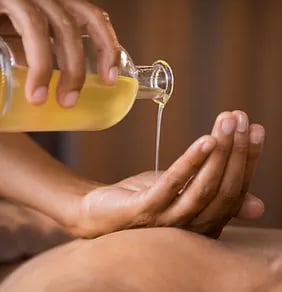 Une personne tient une bouteille d'huile d'un main. Elle verse un filet d'huile dans son autre main.
