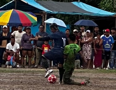 Local soccer players competing on a muddy field during a match in front of a crowd.