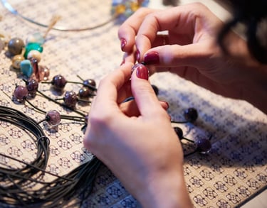 Manos de artista ensamblando un collar de cuentas hecho a mano usando cuentas de vidrio y cordón.