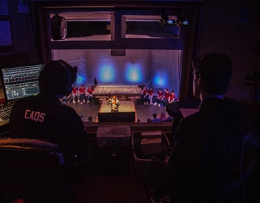 Two figures facing away from the camera looking through a window to the stage
