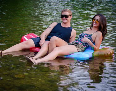 Two people sitting on an inner tube in the lake, wearing protective sunglasses