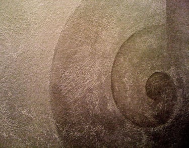 Close-up of a snail swirl painted with warm silver paint in a gritty texture.