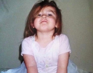 a young girl sitting on a bed with a pink dress