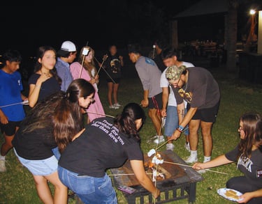 With young people roasting marshmallows outside by a campfire.