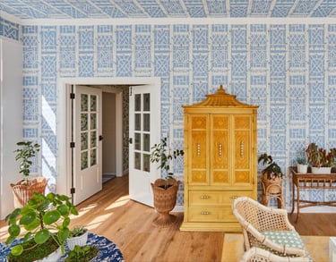 Elegant sunroom featuring blue geometric lattice wallpaper, an ornate yellow Chinoiserie armoire, and lush indoor plants.