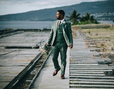 Marié élégant en costume trois pièces vert sauge tenant le bouquet de mariée, marche sur un ponton.