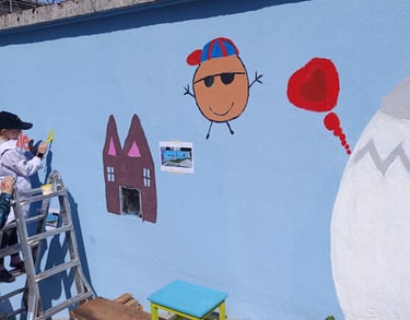 Bambini dipingono figure giocose su muro azzurro durante laboratorio artistico curato da Poliops.