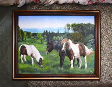 a framed painting of three horses grazing in a field