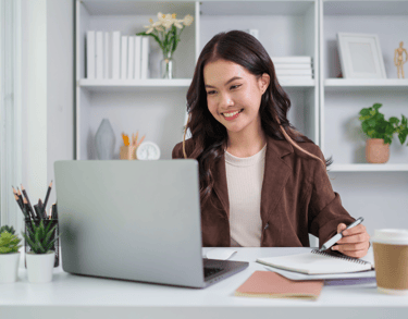 Chica sonriente sentada en un escritorio con un ordenador portátil y una libreta
