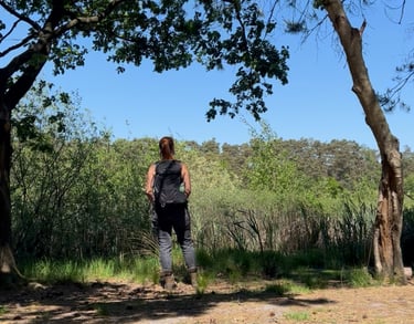 Anneke met rugzak, uitkijkend over een vijver, omringd door bomen