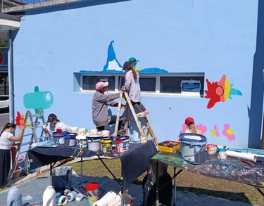 Gruppo di bambini e adulti dipinge insieme su muro azzurro durante laboratorio artistico Poliops.