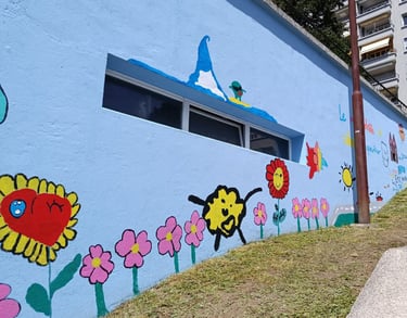 Murales colorato realizzato con bambini, fiori e sole su parete azzurra, progetto artistico colletti