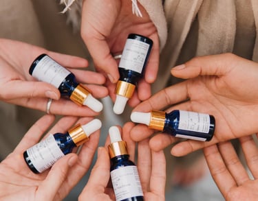 Diverse hands holding organic blue glass dropper bottles with essential oil blends and herbal serums.