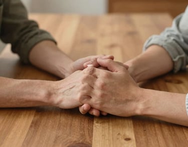 Close-up of two people holding hands across a clean wooden dining table in a North American home, shallow depth of field, warm and supportive atmosphere.