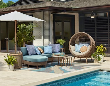 Modern poolside patio featuring a blue outdoor sectional sofa, wicker pod chair, and white sun umbrella.