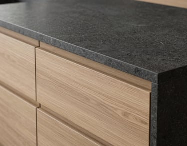 A close-up of a high-end kitchen island with a smooth charcoal stone countertop and minimalist light oak drawers, soft natural light, European interior design style.