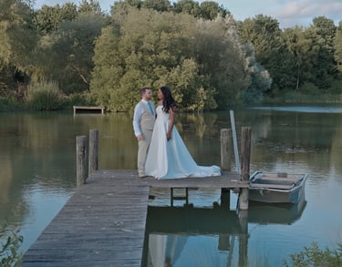 Bride and groom walking along a pier towards a lake.