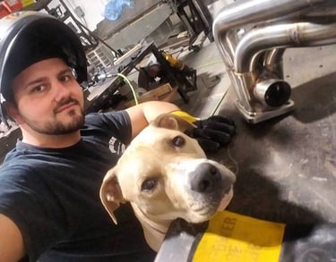 Professional welder with his dog next to a custom fabricated stainless steel exhaust manifold.