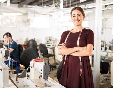 Diseñadora de moda sonriente de pie en una fábrica de ropa con máquinas de coser industriales..