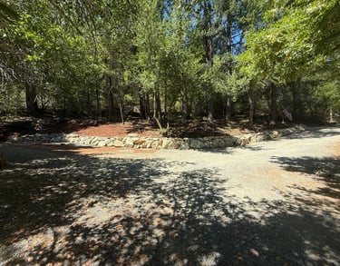 Rock wall with driveway in front and trees behind