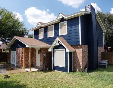 Two-story home with navy blue siding, red brick accents, and a brown shingle roof under a blue sky.