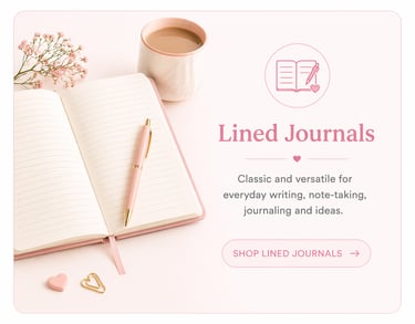 An open pink lined journal on a desk with a gold pen, coffee cup, and flowers for note-taking.