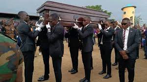 Porteurs en costumes noirs avec un cercueil en bois lors de funérailles à Douala.