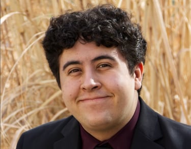 Image of Gregg in a black suit behind is tall grass.