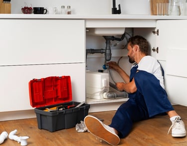 plumber repairing pipes under a kitchen sink in an Auckland home