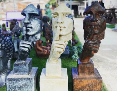 Three silence sculptures in silver, white, and bronze displayed in an outdoor garden decor shop.