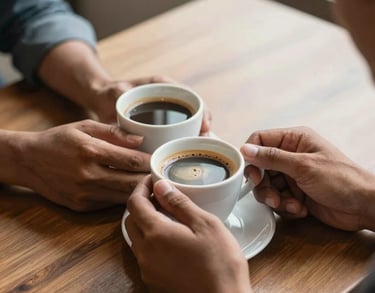 A close-up shot of two South Asian hands holding a warm cup of coffee during a conversation on a wooden table, emphasizing connection and support, soft morning light.