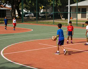 An outdoor multi-sports court with soft green fences, vibrant orange markings, and young children in sports gear, South American setting.