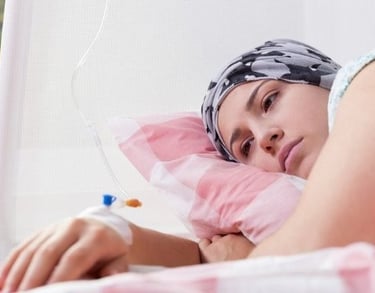 A female cancer patient wearing a headscarf lies in a hospital bed receiving chemotherapy treatment via an IV drip.