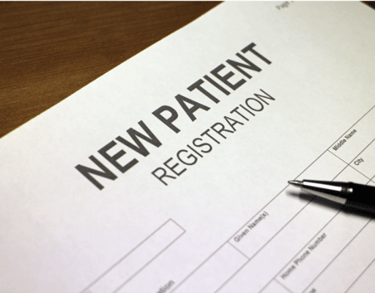A black pen resting on a medical new patient registration form on a wooden desk.