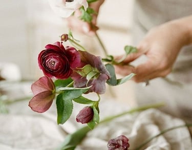 Florista sosteniendo una rosa roja sobre mesa de lino claro.
