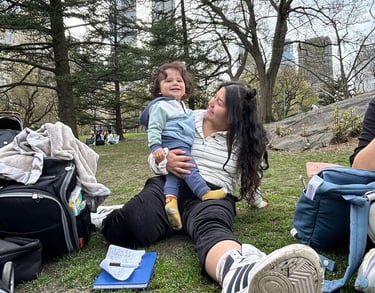 A mother holding her toddler while sitting on the grass in Central Park.