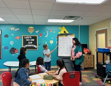A primary student leads an alphabet lesson for a group of children in a colorful elementary classroom.