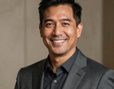 A professional headshot of a North American man with a warm smile, wearing a dark slate gray suit, set against a blurred beige background.
