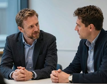 A photo of two professionals in a Northern European setting, engaged in a focused but calm conversation across a table, emphasizing a supportive and empathetic atmosphere with soft blue accents.