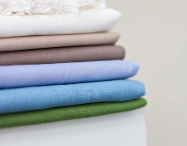 Close-up of a neatly stacked pile of folded fabric swatches in various neutral and pastel colors, including white, beige, bro