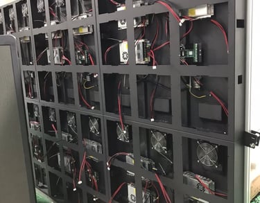 Rear view of an LED display panel wall showing internal wiring, power supplies, and cooling fans.